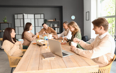 Wall Mural - Business colleagues having lunch at table in office kitchen