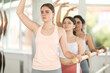 © JackF - Motivated young female ballet student mastering third position at barre with group of fellow amateur dancers standing with arms gracefully arched above heads in bright choreography studio