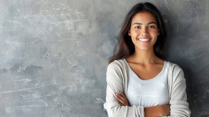 Wall Mural - A young Hispanic woman with long dark hair and a pleasant smile stands with her arms crossed in front of a gray wall. Generative AI