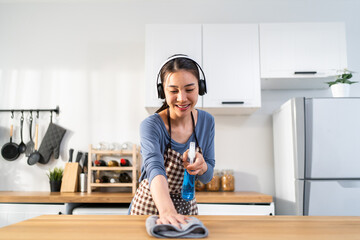 Sticker - Asian young woman cleaner wearing headphones cleaning kitchen at home.