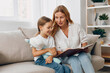 © SHOTPRIME STUDIO - Mother and daughter bonding time enjoying a storybook together on a cozy living room couch, sharing smiles and laughter