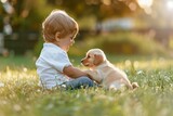 Little child in white shirt and jeans sitting on grass playing with puppy