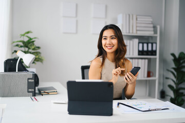 Wall Mural - Confident Asian Business Woman Working in Modern Office with Smartphone and Tablet