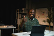© Parichat - African American Man Smiling and Giving Thumbs Up While Working on Laptop in Modern Office Setting
