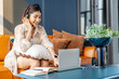 © TeTe Song - Consultant girl wearing headset with microphone sitting on sofa,, freelance worker, call center or support service operator helpline. Young woman having talk with client or colleague and take notes