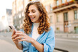 © maxbelchenko - Smiling young woman walking around old street and using smartphone. Communication, social networks, blogging, online shopping concept.