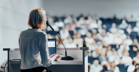 Wall Mural - Female speaker giving a talk on corporate business conference. Unrecognizable people in audience at conference hall. Business and Entrepreneurship event