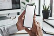 © ttonaorh - Mockup of a man's hands holding smart phone with blank white screen while sitting at the wooden table in modern office