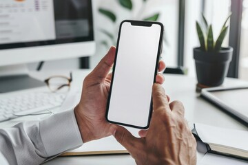 Mockup of a man's hands holding smart phone with blank white screen while sitting at the wooden table in modern office
