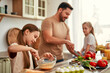 © Valerii Apetroaiei - Happy Family Cooking in Kitchen: Father and Children Prepping Vegetables and Baking