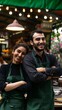 © VISUAL BACKGROUND - A smiling couple in green aprons standing in front of a restaurant.