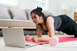 © itchaznong - Overweight Woman Engaging in Home Workout for Wellness and Fitness with Laptop and Dumbbell