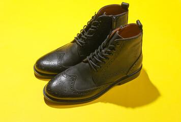 Wall Mural - Stylish black leather men's brogue boots on yellow background with shadow.