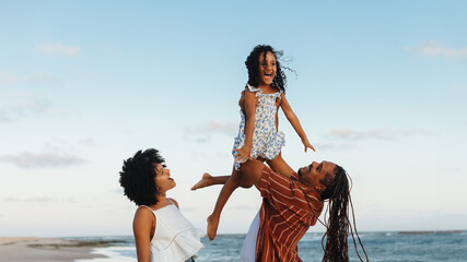 Wall Mural - Happy family enjoying a beach vacation with parents lifting child in the air