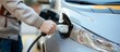 © Yana - The driver of the electric car inserts the electrical connector to charge the batteries. A hand of a man attaching power cable to electric car. Electric vehicle. Charging your electromobile.