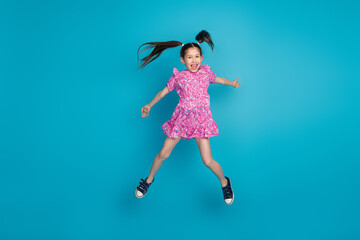 Poster - Full length photo of adorable lovely small girl wear pink dress jumping high empty space isolated blue color background