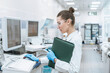 © illustrissima - A female scientific researcher conducts a series of experiments in a modern bio laboratory with test tubes and a pipette. Doctor with folder of papers with tablet in laboratory