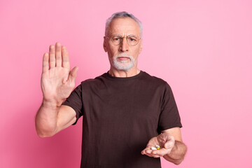 Wall Mural - Portrait of serious senior man with beard dressed brown t-shirt in glasses give you pills show palm isolated on pink color background