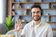 © Tetiana - Close-up photo of a young Muslim man wearing glasses and a headset at home, talking and greeting the camera