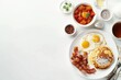© Mamstock - A top down view of a full American breakfast on a white background with plenty of space for additional images The breakfast includes sunny side up fried eggs crispy bacon hash browns fluffy pancakes