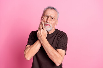 Wall Mural - Portrait of suffering man with beard dressed t-shirt in glasses hold both hands on cheek have teeth ache isolated on pink color background