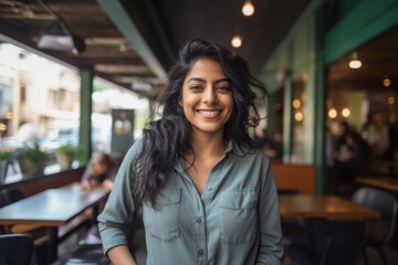 Wall Mural - Portrait of a grinning indian woman in her 20s sporting a breathable hiking shirt over bustling city cafe