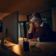 Poster - Stress, night and mature businesswoman at desk by computer for fatigue, overtime or project deadline in office. Headache, publishing agency and employee for exhausted, burnout or eye strain in dark