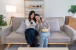 © Natee Meepian - Cozy Lesbian Couple Relaxing on Sofa and Watching TV Together in Modern Living Room