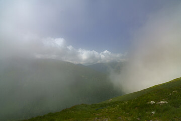 Wall Mural -  A panorama of a grass-covered hill with mountains behind and clouds above