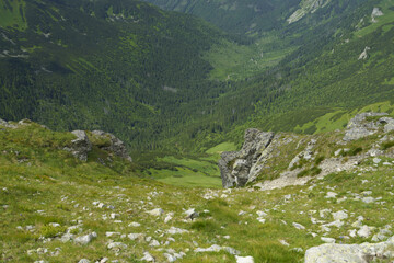 Canvas Print -  A valley nestled among mountains, flanked by rocky cliffs and verdant grassy expanses