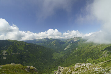 Wall Mural -  A valley viewed with mountains distantly, clouds in the sky above, and clouds in the foreground