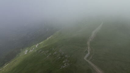 Canvas Print -  A birds-eye perspective of a misty mountain featuring a winding path ascending its slope in the foreground