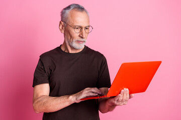 Wall Mural - Portrait of serious focused man with beard dressed brown t-shirt in glasses look at laptop read email isolated on pink color background