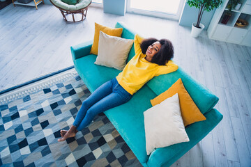 Wall Mural - Photo of dreamy cute girl sitting on sofa holding arms behind head in comfy room day light indoors