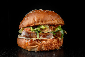 Wall Mural - Close-up of a juicy burger with fresh lettuce and sauce on a sesame seed bun against a dark background