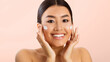 © Prostock-studio - Asian young woman with dark hair applying white face cream to her cheeks, smiling at the camera. She has a fresh, clean complexion and appears to be enjoying the process of applying the cream