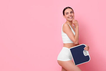 Wall Mural - Diet and weight loss concept. Happy young woman with floor scale on pink background. Space for text