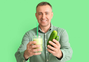 Canvas Print - Mature man with glass of vegetable smoothie and cucumbers on green background