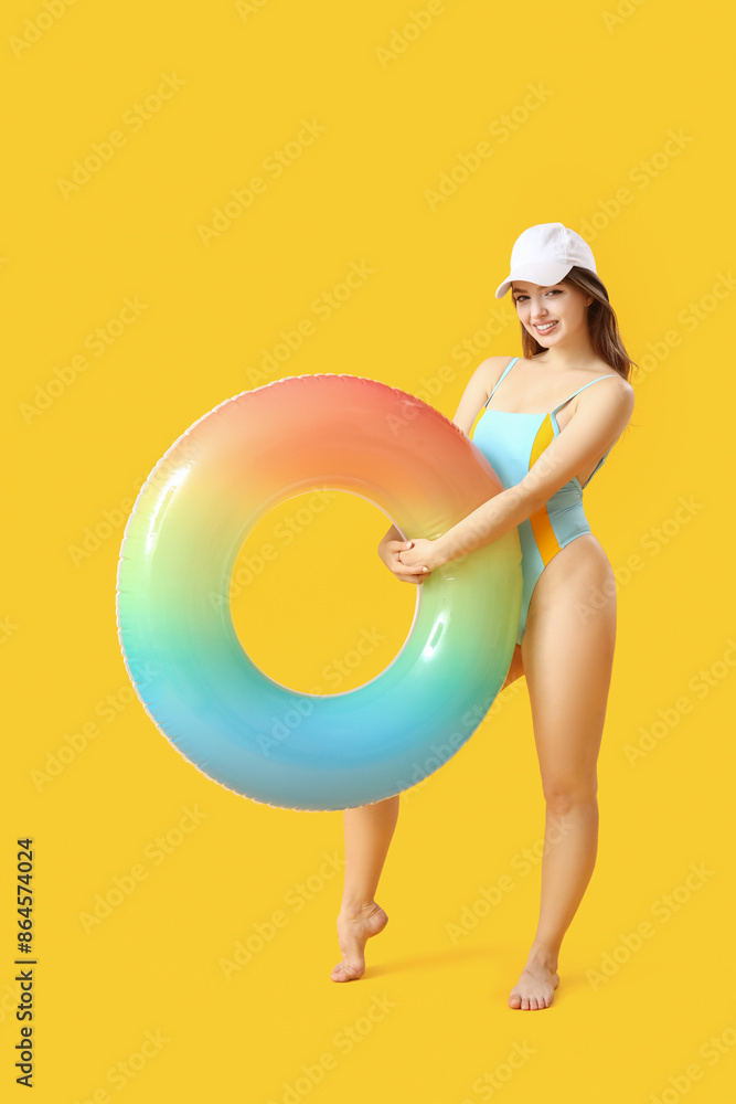 Young woman with swim ring on yellow background