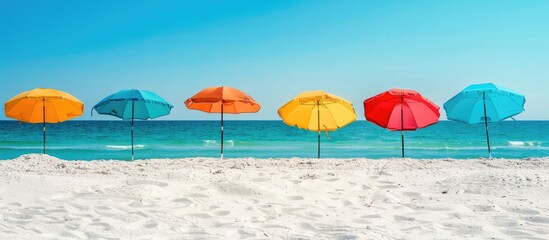 Wall Mural - Colorful umbrellas on the sandy beach by the ocean, against a backdrop of clear blue sky, offering an inviting copy space image.