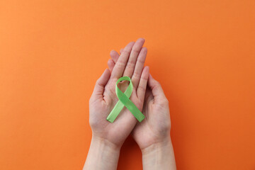 Wall Mural - Woman with light green awareness ribbon on orange background, top view