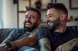© ArtCraft - Happy gay couple relaxing at home. Two men laughing together on a comfortable couch, expressing joy and companionship. Ideal for lifestyle, relationship, and inclusivity themes.