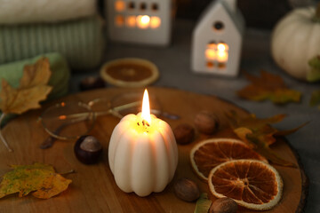 Wall Mural - Wooden board with burning candle and autumn decor on table, closeup