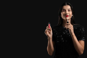 Wall Mural - Beautiful young woman applying red lipstick on black background