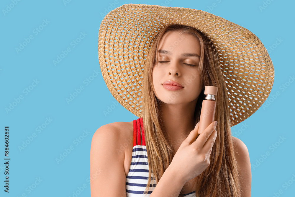 Young woman in straw hat with perfume on blue background, closeup