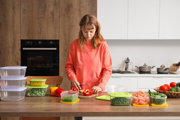 Wall Mural - Young woman cutting bell pepper for freezing on wooden table in kitchen