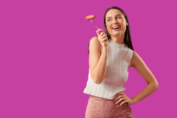 Young woman with tasty sausage on purple background