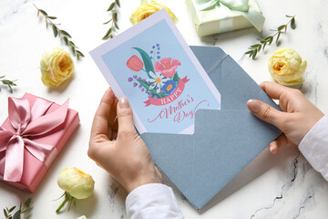 Canvas Print - Female hands with festive postcard, gift boxes and flowers on white grunge background. Happy Mother's Day