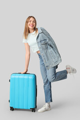 Poster - Beautiful young woman with blue suitcase on grey background