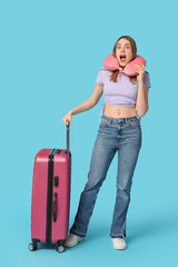 Canvas Print - Shocked young woman with suitcase and neck pillow on blue background